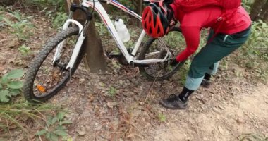 Kırmızılı kadın ormanda bisikletini tamir ediyor.