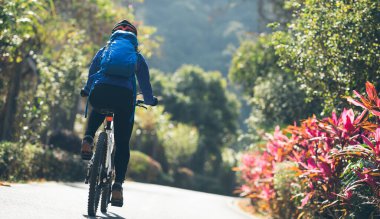 Baharda tropik park yolunda bisiklet süren bir kadın.