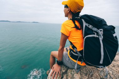 Korkusuz kadın yürüyüşçü deniz kenarındaki uçurumun kenarında oturur.
