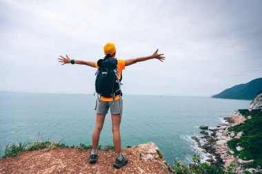 Başarılı yürüyüşçü, deniz kıyısındaki dağın yamacında kollarını açmış.