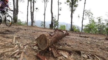 Bisikletli bir kadın dağın tepesinde orman yolunda bisiklet sürüyor.