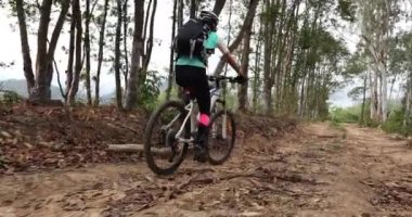 Bisikletli bir kadın dağın tepesinde orman yolunda bisiklet sürüyor.