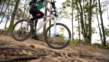 Bisikletli bir kadın dağın tepesinde orman yolunda bisiklet sürüyor.