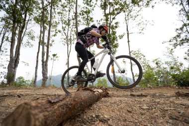 Bisikletli bir kadın dağın tepesinde orman yolunda bisiklet sürüyor.