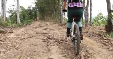 Bisikletli bir kadın dağın tepesinde orman yolunda bisiklet sürüyor.