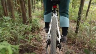 Bisikletli bir kadın dağın tepesinde orman yolunda bisiklet sürüyor.