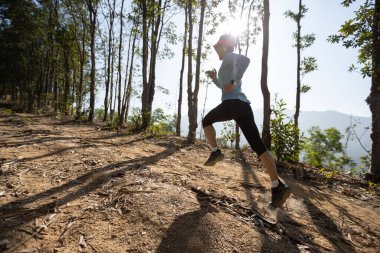 Gündoğumunda tropikal dağ zirvesinde koşan genç bir kadın koşucu.