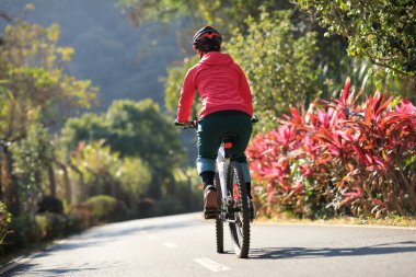Baharda tropik park yolunda bisiklet süren bir kadın.