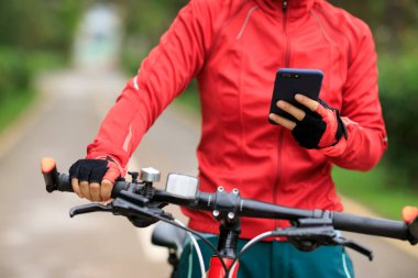 Bisikletçi orman yolunda dağ bisikleti sürerken akıllı telefon kullanır