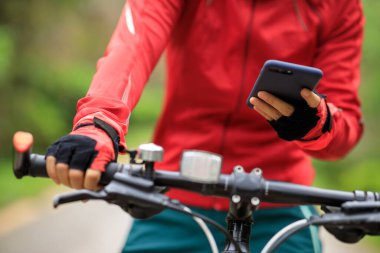 Bisikletçi orman yolunda dağ bisikleti sürerken akıllı telefon kullanır
