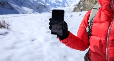 Sırt çantalı bir kadın kışın akıllı telefonuyla kar dağlarının fotoğrafını çekiyor.