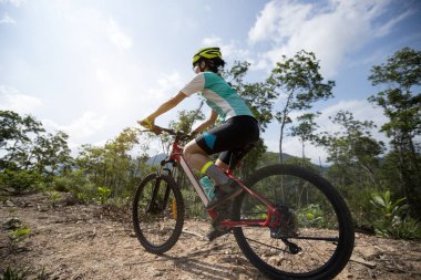 Bisikletli bir kadın dağın tepesinde orman yolunda bisiklet sürüyor.