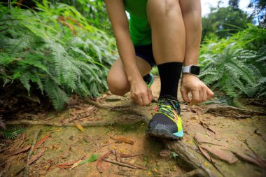 Orman yolunda ayakkabı bağı bağlayan kadın koşucu.