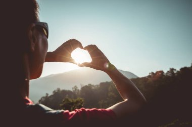 Başarılı kadın ellerinin silueti gündoğumu dağının tepesinde kalp şekli oluşturuyor.