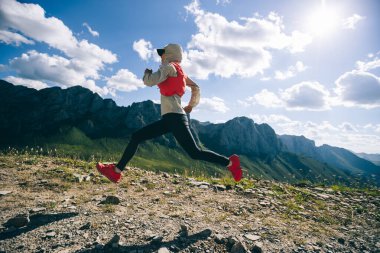 Genç kadın ultra-maraton koşucusu dağın tepesinde koşuyor.