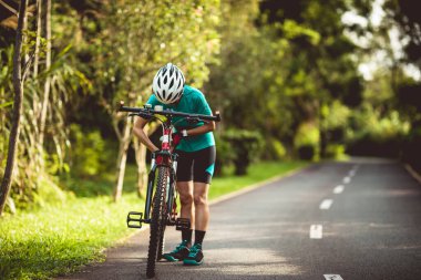 Bisikletli kadın, yaz parkında bisiklet sürerken koltuk yüksekliğini ayarlıyor.