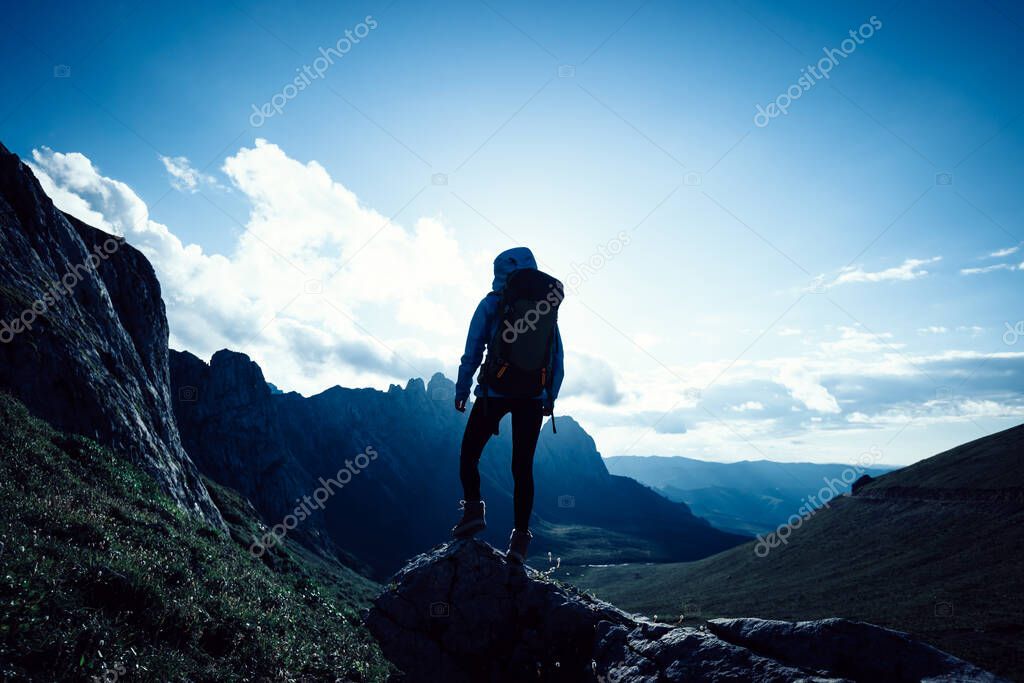 Successful woman backpacker hiking on sunset alpine mountain top