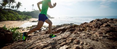 Gün doğumunda kayalık dağın tepesine koşan kadın koşucu.