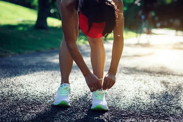 在阳光灿烂的热带公园小径上系鞋带的女跑步者 — 图库照片