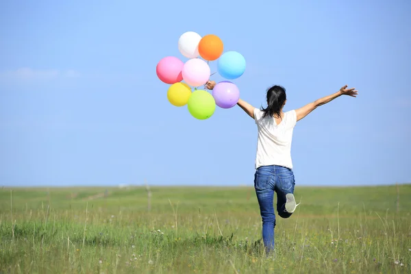 Ung asiatisk kvinna körs på grön Vall med färgade ballonger — Stockfoto