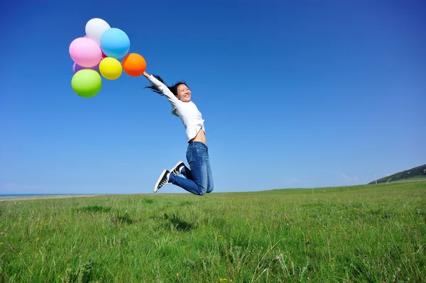 Jonge Aziatische vrouw springen op groene grasland met gekleurde ballonnen — Stockfoto