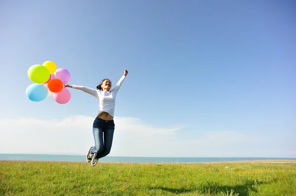 Junge Asiatin springt mit bunten Luftballons auf grüne Wiese — Stockfoto