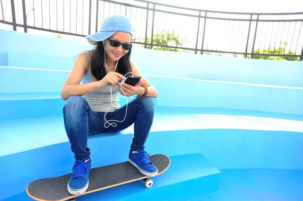 Kvinna skateboardåkare sitta på skatepark trappor lyssnar musik från smart telefon mp3-spelare — Stockfoto