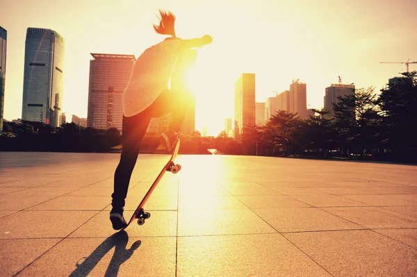 Žena skateboarder skateboarding při východu slunce města — Stock fotografie