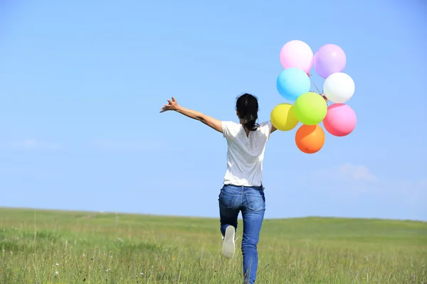 Joven mujer asiática corriendo y saltando en verde pastizal con globos de colores —  Fotos de Stock