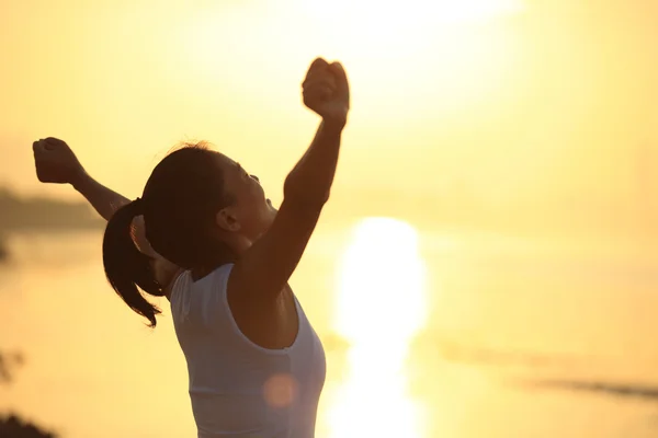 Vrouw open armen onder de zonsopgang op de zee — Stockfoto