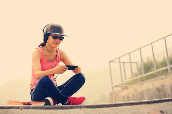 Woman skateboarder listening music from smart phone — Stock Photo, Image