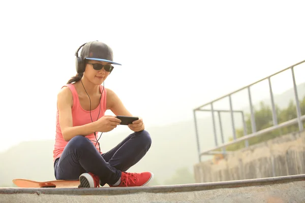 Vrouw skateboarder luisteren muziek van slimme telefoon — Stockfoto