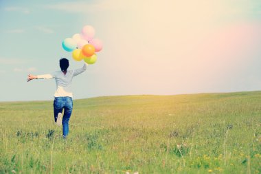 Genç Asyalı kadın koşma ve atlama üzerinde renkli balonlar ile yeşil otlak