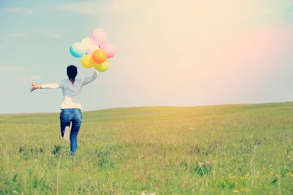 Young asian woman running and jumping on green grassland with colored balloons — Stock Photo, Image
