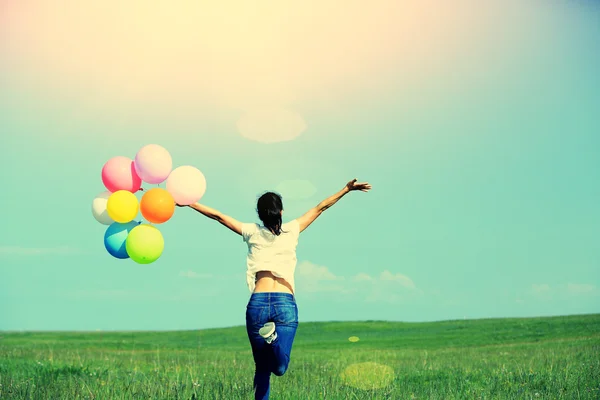Молода азіатка біжить і стрибає на зелених луках з кольоровими кульками — стокове фото