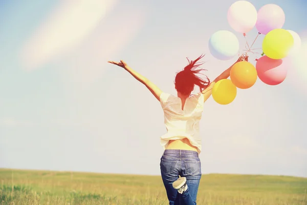 Jeune femme asiatique courir et sauter sur la prairie verte avec des ballons colorés — Photo