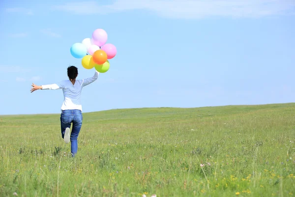 年轻的亚裔女子跑步和跳跃着彩色气球的绿色草原上 — 图库照片