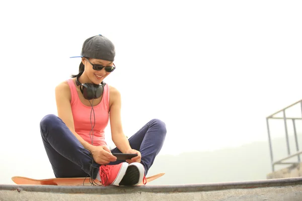 Mujer skateboarder escuchar música desde el reproductor de mp3 teléfono inteligente —  Fotos de Stock