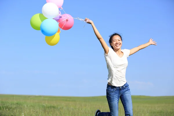 Jonge Aziatische vrouw uitgevoerd en springen op groene grasland met gekleurde ballonnen — Stockfoto