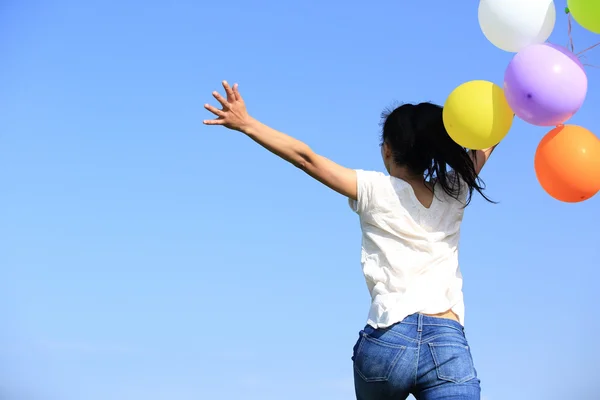 Jeune femme asiatique courir et sauter sur la prairie verte avec des ballons colorés — Photo