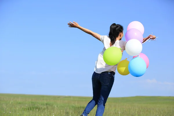 Jovem mulher asiática correndo e pulando em pastagens verdes com balões coloridos — Fotografia de Stock