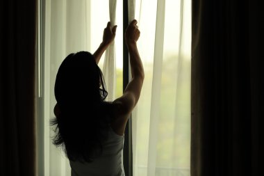 Genç kadın yatak odasında perdeleri açmayı