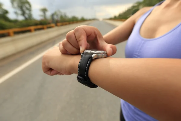 Young woman jogger looking at sports smart watch, checking performance or heart rate pulse trace