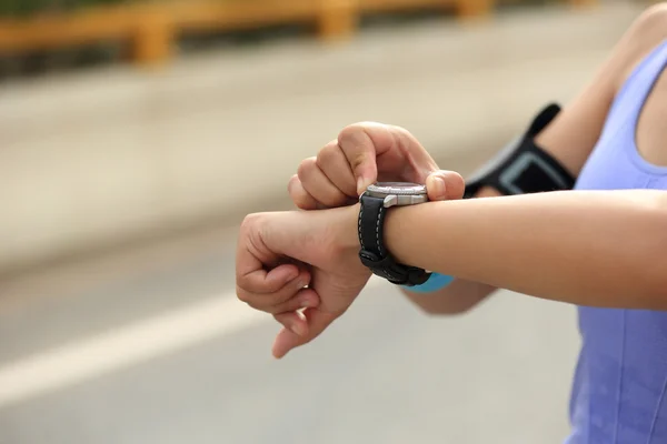 Young woman jogger looking at sports smart watch, checking performance or heart rate pulse trace. Sport and fitness outdoors in city.