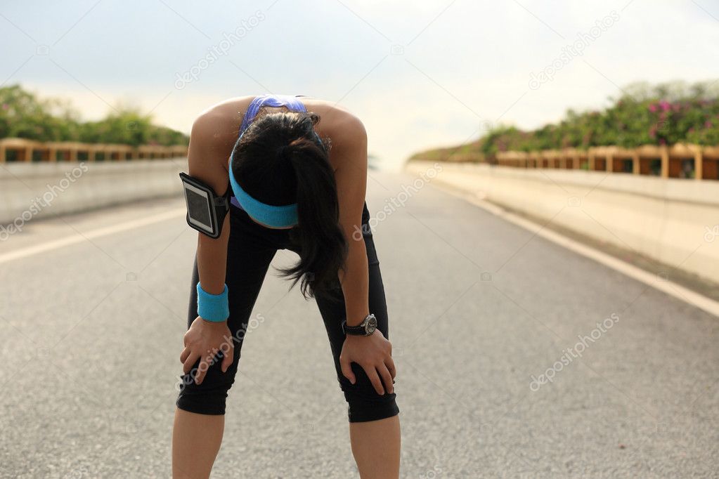 Tired woman runner taking rest after running hard on city road