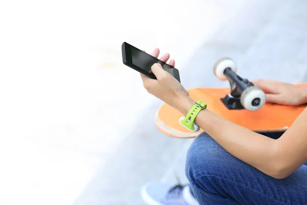 在城市中使用智能手机近距离观察年轻女子滑板者 — 图库照片