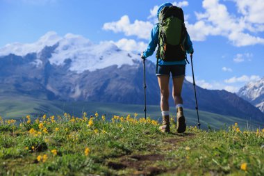Sırt çantalı bir kadın çiçek açan çayırların tepesinde yürüyüş yapıyor.