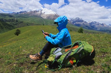 Otlakta akıllı telefon kullanan sırt çantalı bir kadın. 