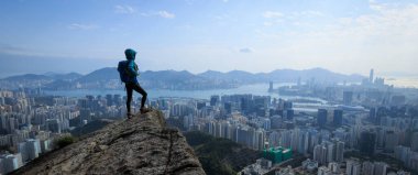 Hong Kong 'da dağ yamacına tırmanan sırt çantalı adam, şehir mimarisinde nefes kesici bir manzara. 