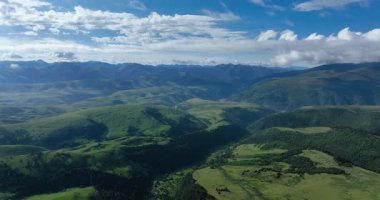 Beyaz bulutlu mavi gökyüzünün altında yuvarlanan yeşil dağların insansız hava aracı görüntüleri..